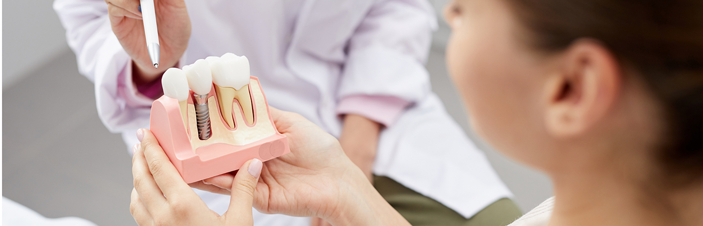 Close-up of dentist pointing to dental implant model held by patient