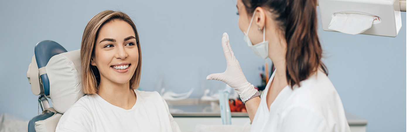 Woman in dental chair talking to female dentist wearing a glove